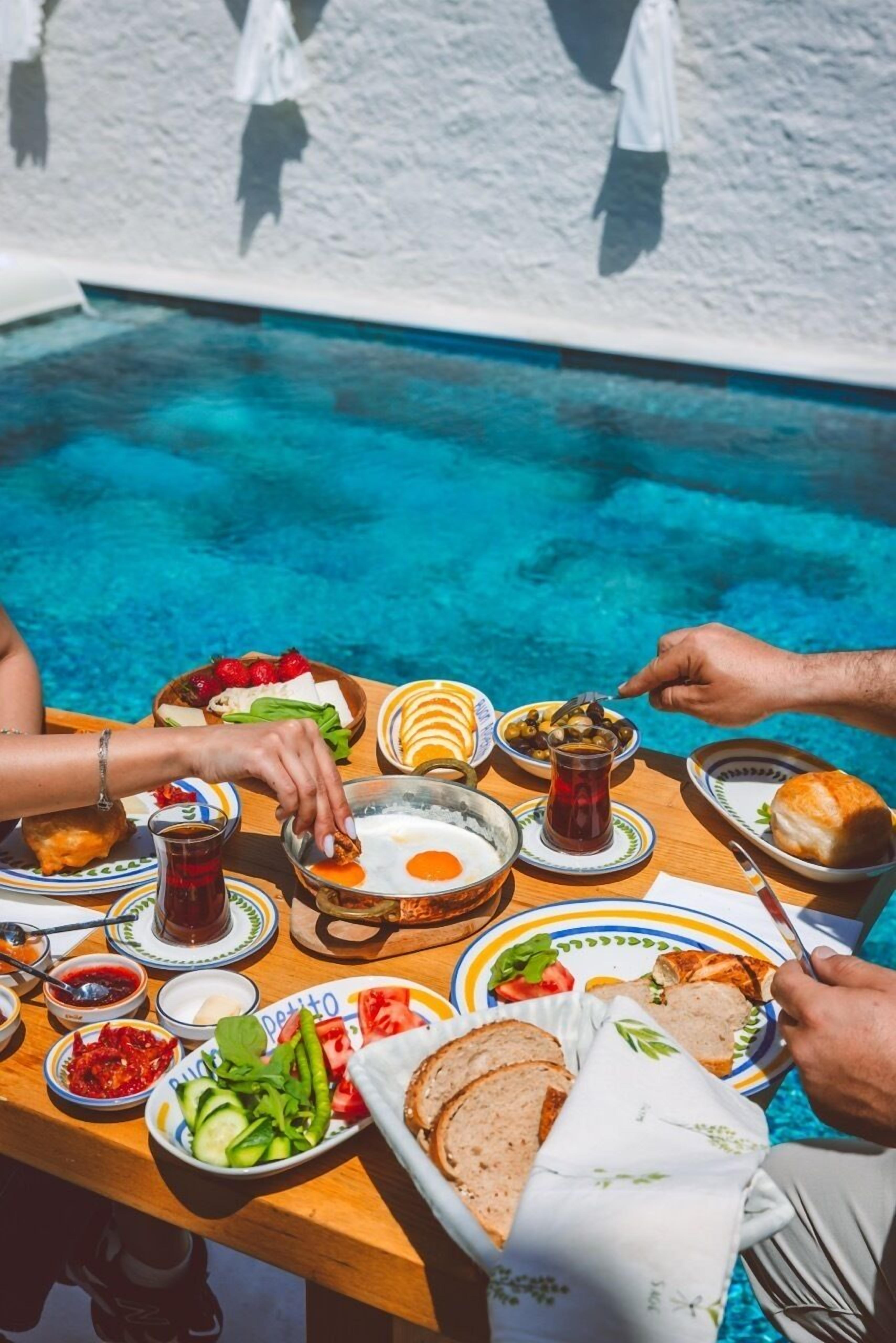 Une table à manger avec différents plats, une piscine et un mur blanc en arrière-plan.