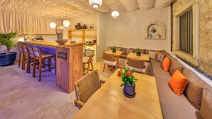 Una zona de recepción con mostrador de madera, sillas, un sofá y una mesa de comedor con planta en maceta.