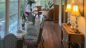 Una habitación amplia con una mesa larga, sillas, un ventilador de techo y ventanas grandes.