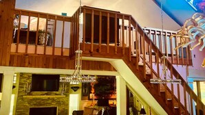Un interior de madera con varios niveles, una escalera, un candelabro y un ventanal grande.