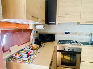 A kitchen with wooden cabinets, a gas stove, a microwave, and a tiled backsplash. - Luigina's Home • Direct Metro to the Vatican, Terrace & Parking (Roma)