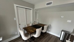 A dining area with a wooden table and four chairs, a trash can, and a door with a vent. - Cozy 1-bedroom apartment in beautiful Virginia Beach with AC (Virginia Beach)