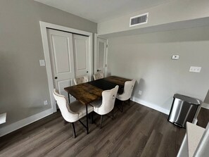 A dining area with a wooden table and four chairs, a trash can, and a door with a vent. - Cozy 1-bedroom apartment in beautiful Virginia Beach with AC (Virginia Beach)