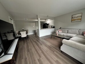 A modern living room with a sofa, TV, dining table, and kitchen area.