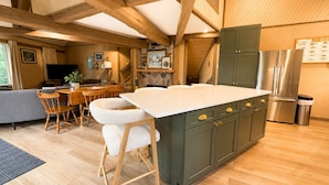 A spacious kitchen with wooden beams, a central island, and a dining area with chairs and a table. - Hexagon Hideaway on Balsam Lake • Private Dock • Kayaks • Sunset Views (Balsam Lake)