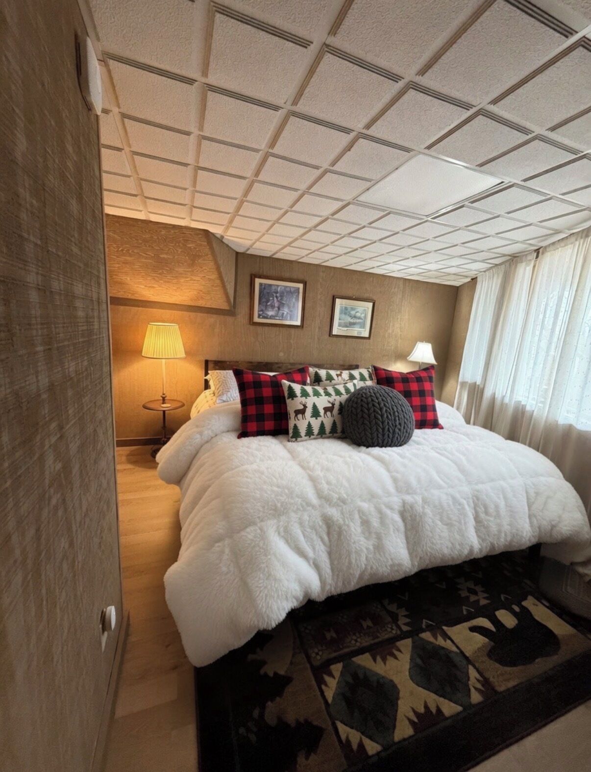 Una habitación de hotel con una cama grande, un cabecero, una mesita de noche con lámpara y una alfombra estampada.