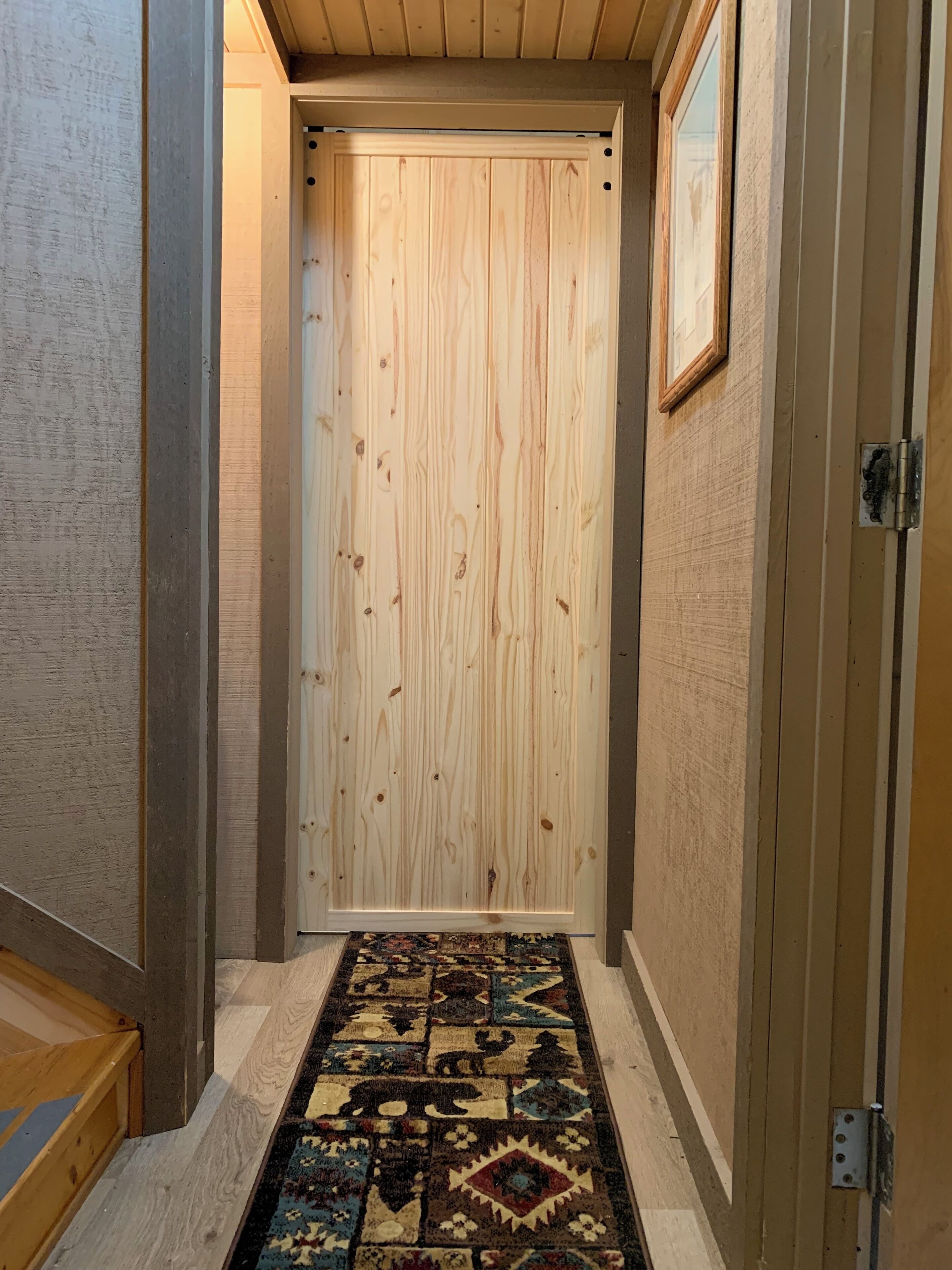 Un pasillo con una puerta de madera, un tapete estampado y un cuadro en la pared.
