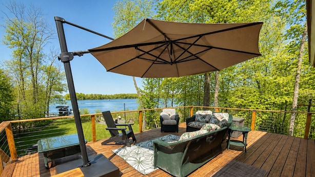 A deck with outdoor furniture, a table, and an umbrella. - Hexagon Hideaway on Balsam Lake • Private Dock • Kayaks • Sunset Views (Balsam Lake)
