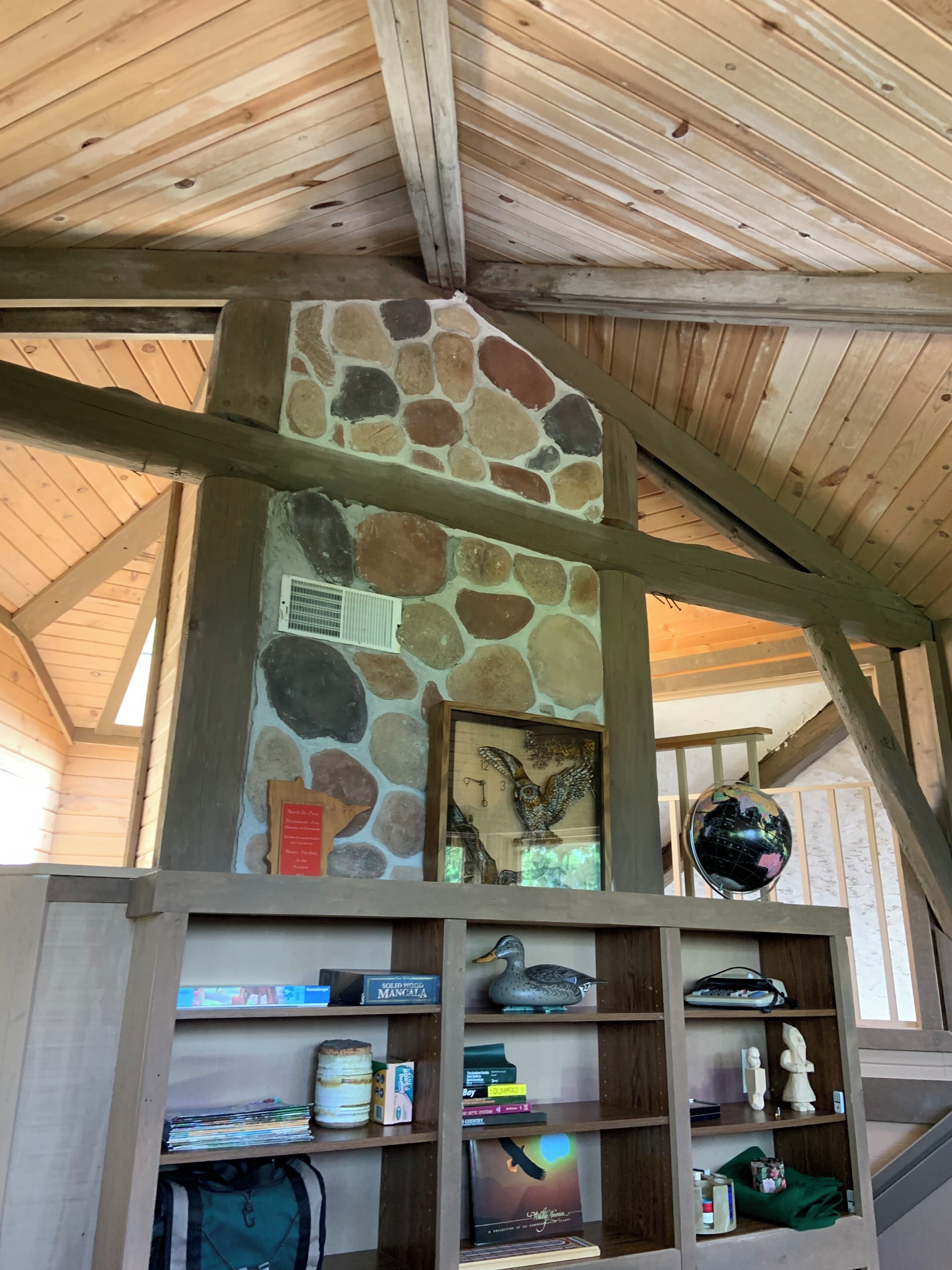 A room with a stone wall, wooden beams, a globe, and shelves with various items.