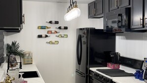 A modern kitchen with dark cabinetry, a stainless steel refrigerator, a built-in oven, and a microwave. - DivineComfort (Newark)