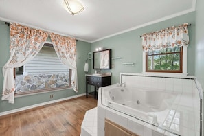 A bathroom with a stone wall, a bathtub, a sink, and a window with floral curtains. - Vista Ridge at Alpine 4bdr (Jasper)