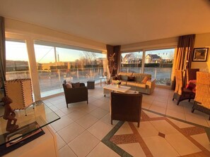A spacious living room with large windows, a sofa set, a coffee table, and a decorative chair. - Seadream view, terraces, 150 m from sea, stores, restaurants, beach bars- parking (Nieuwpoort-Bad)