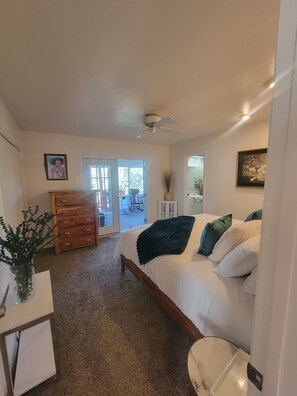 A bedroom with a bed, a dresser, a chair, a vase, and a door leading to a balcony.