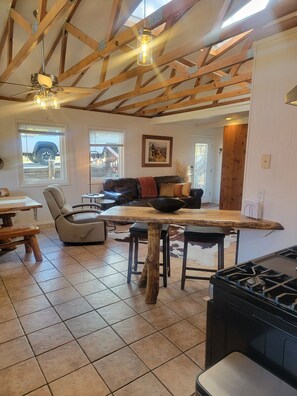A rustic kitchen with a wooden ceiling, a dining area with a leather couch, and a large window.