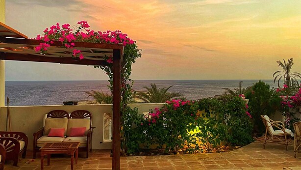 Een zwembadterras met uitzicht op zee, een pergola met bloemen en buitenmeubilair.