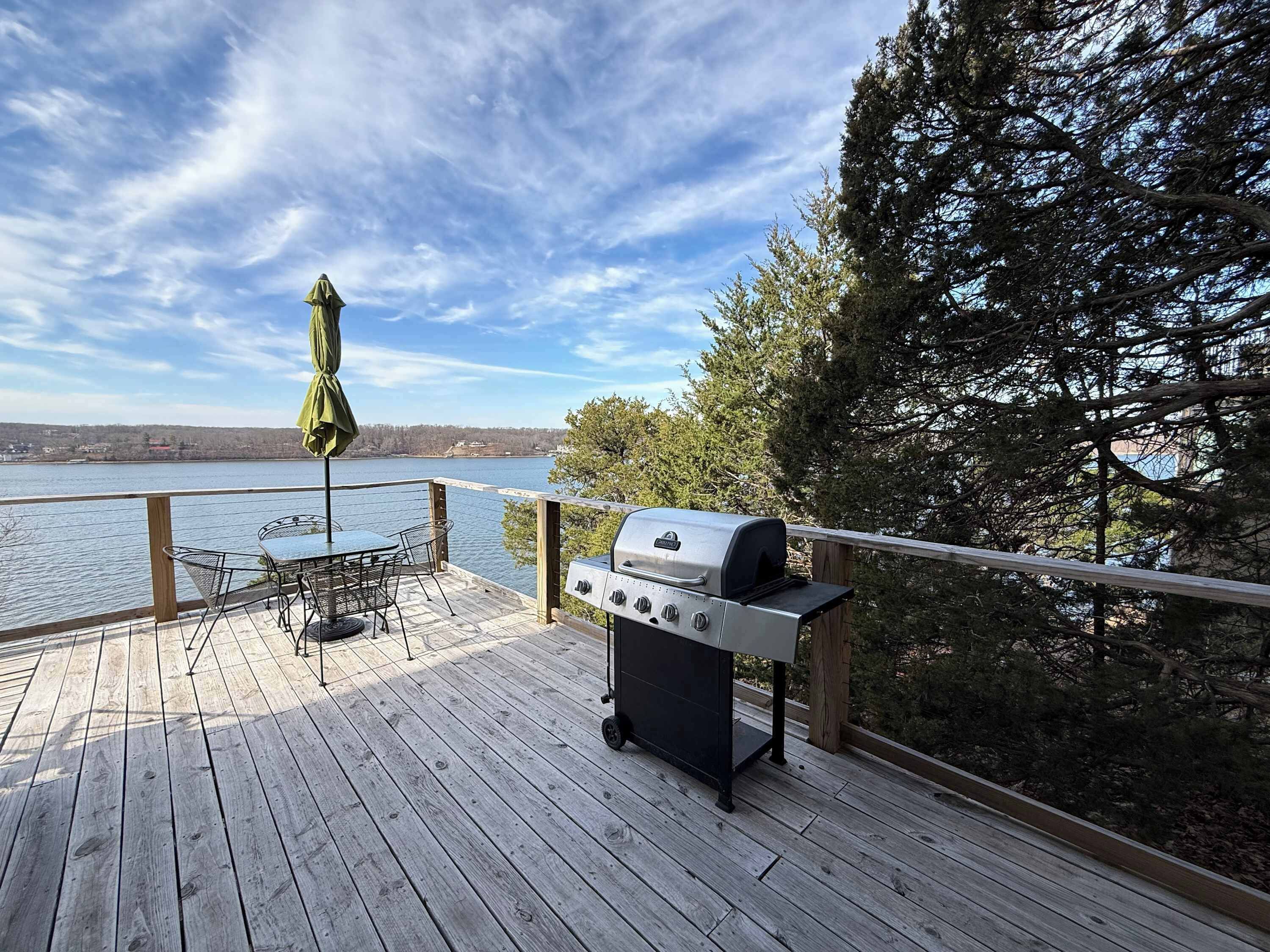 A wooden deck with a grill, a table with chairs, and an umbrella.