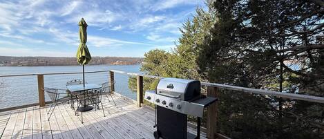 A wooden deck with a grill, a table with chairs, and an umbrella.