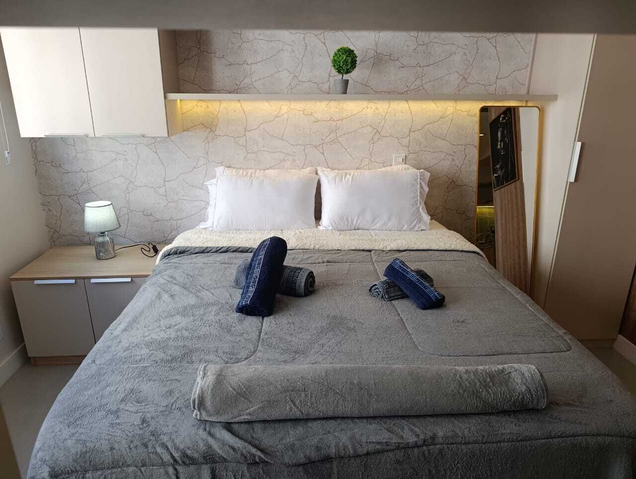A neatly made bed with pillows, a bedside lamp, and rolled towels on a nightstand.
