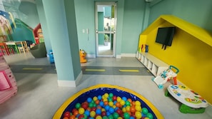Een kinderspeelruimte met een bällebad, kleurrijke speeltoestellen en een geel speeltuintje.