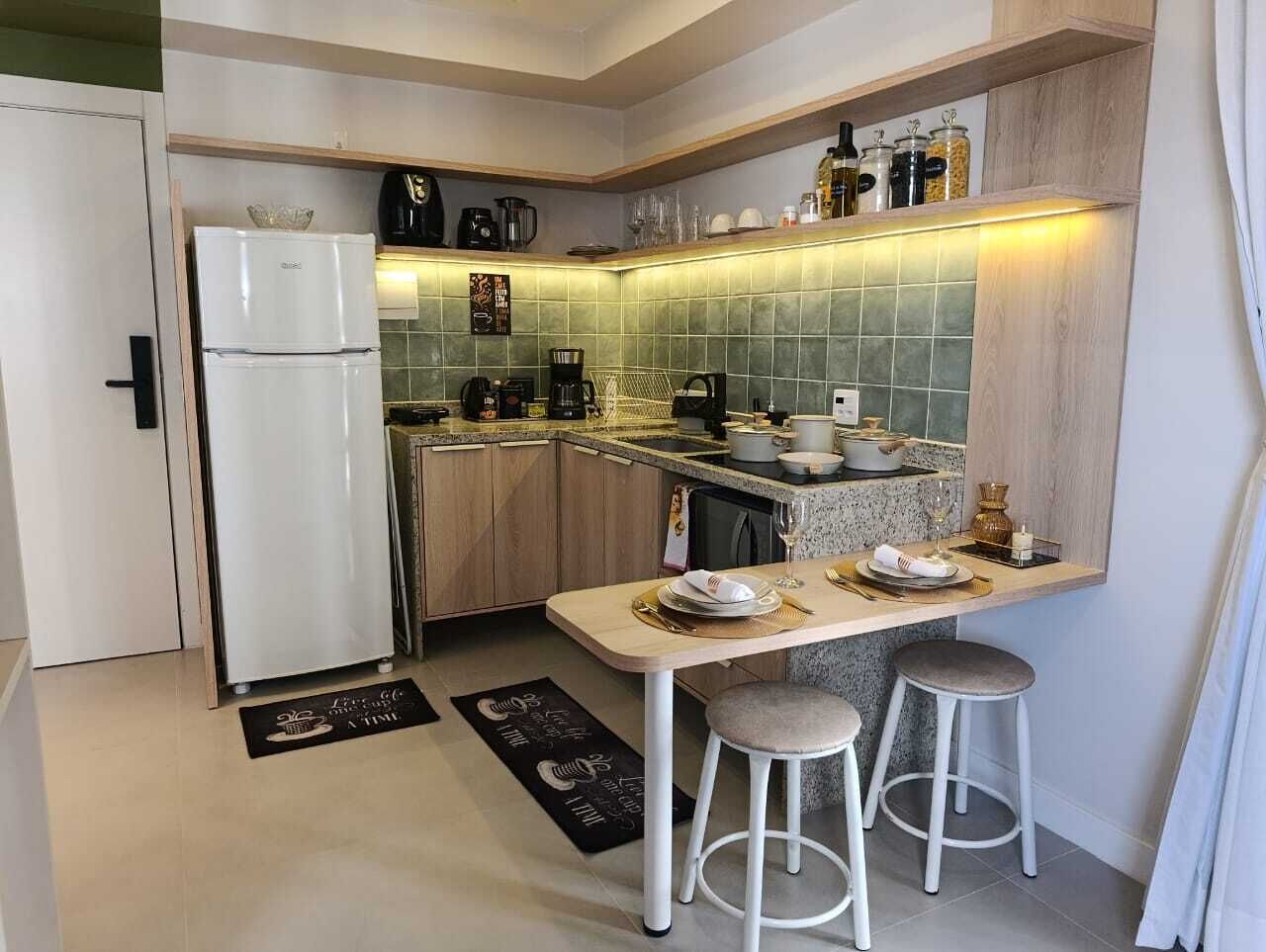 Uma cozinha compacta com geladeira, cafeteira e área de refeições com banquetas.