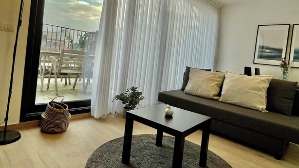 A living room with a sofa, a small table, a lamp, and a view through a window with curtains. - Chic Antwerp Oasis Near Diamond Hub (Antwerp)