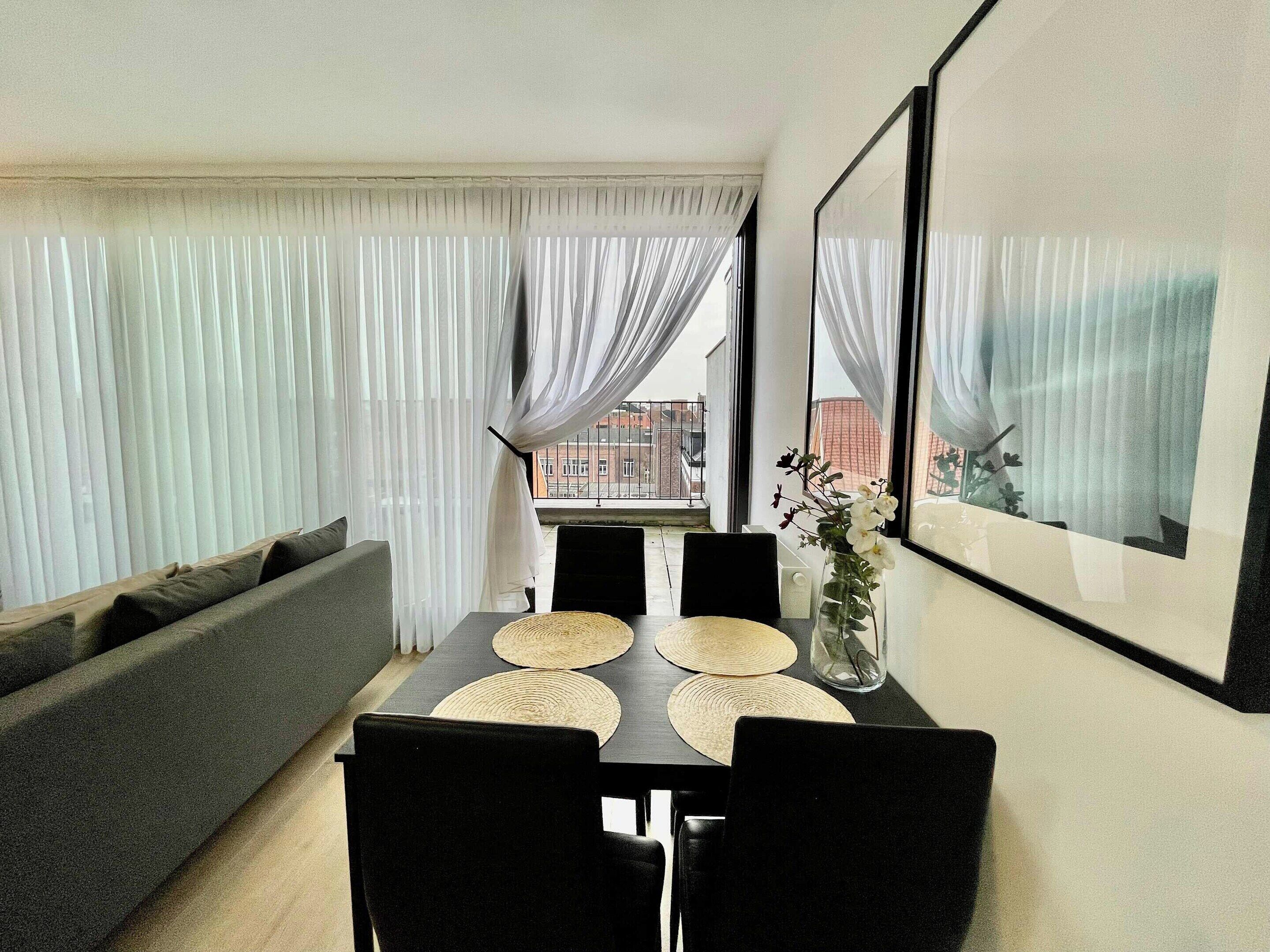 A dining area with a table, chairs, a vase with flowers, and a sofa.