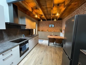 A kitchen with a brick wall, wooden ceiling beams, a black refrigerator, and a wooden dining table with chairs. - The hidden courtyard - the theater (zellwiller)