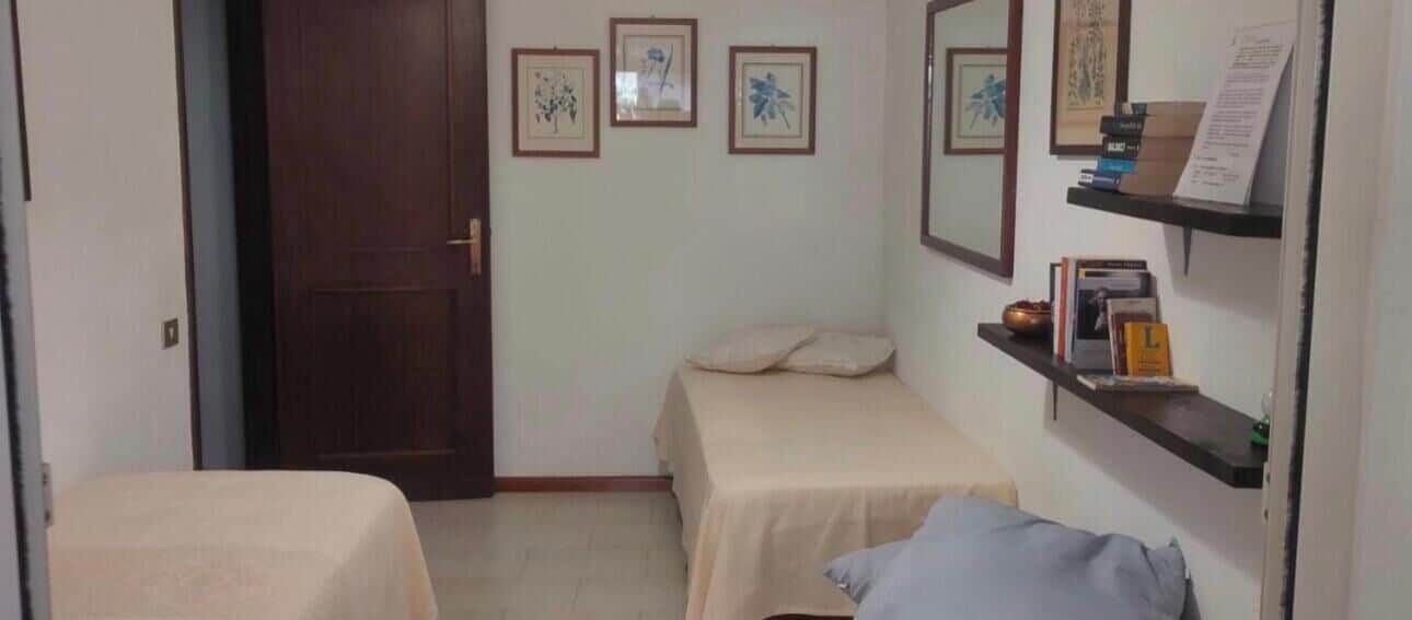Ein Zimmer mit zwei Betten, einer Tür und Regalen an der Wand mit Büchern und einem gerahmten Bild.