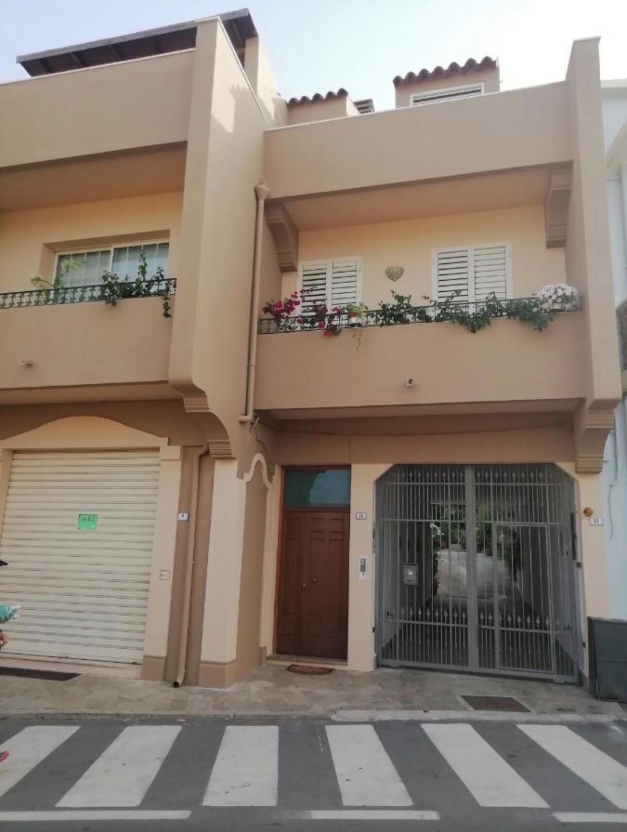 Un edificio de dos pisos con puerta de garaje, entrada con portón y balcón con plantas.