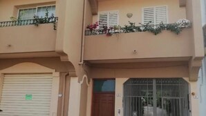 Un bâtiment à deux étages doté d’une porte de garage, d’une entrée fermée par un portail et d’un balcon agrémenté de plantes.
