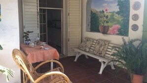 Une terrasse avec des chaises en osier, une table, un banc et une fresque murale.