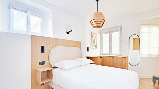 Ein modernes Schlafzimmer mit einem Bett, Nachttischen, einer Hängeleuchte, einem Fenster und einem Spiegel.
