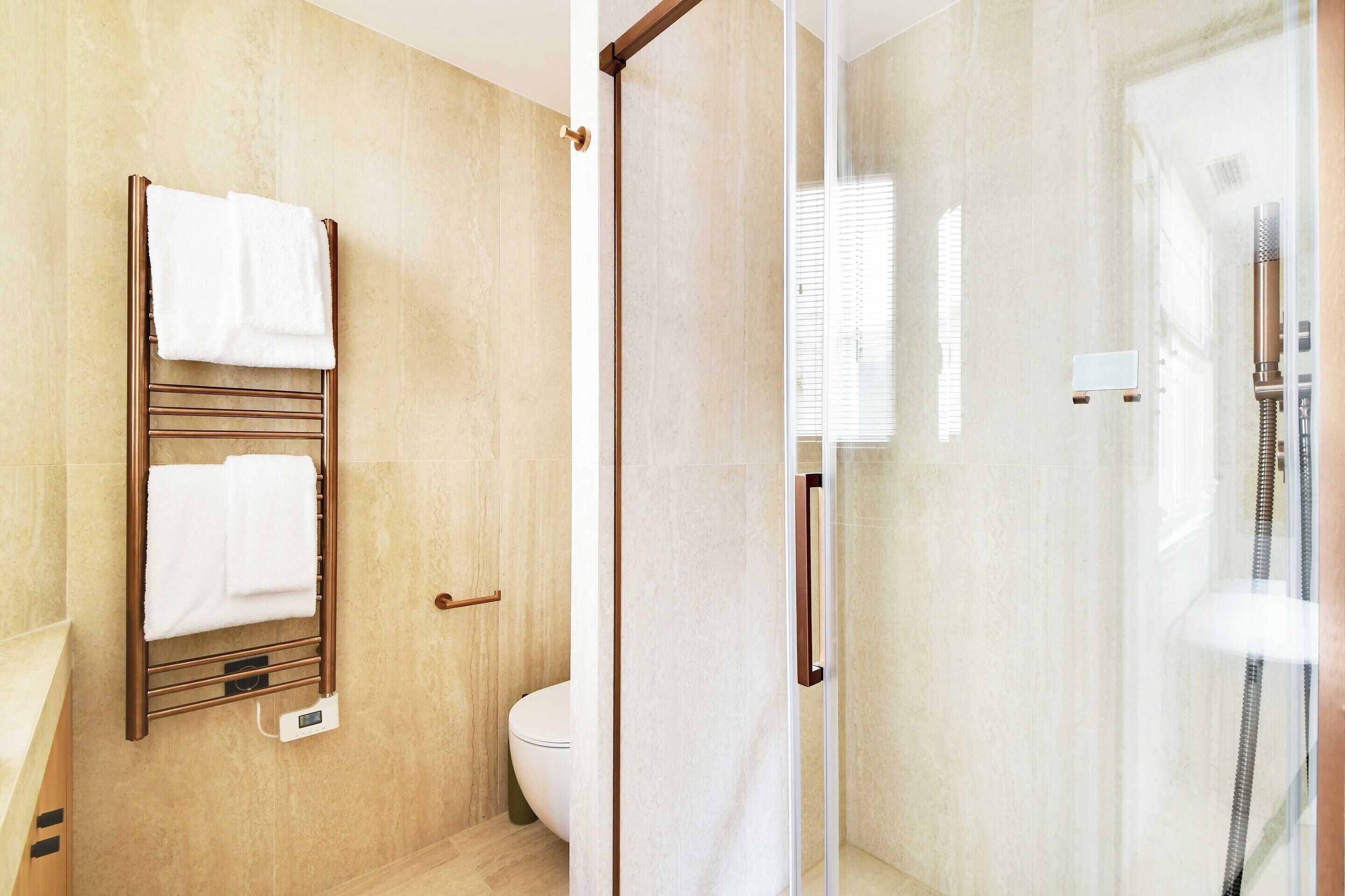 Un baño con ducha envuelta en cristal, un perchero con toallas y un inodoro.