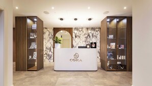 A reception desk with a logo, a potted plant, and shelves with items. - Palace Hotel Città (Arco)