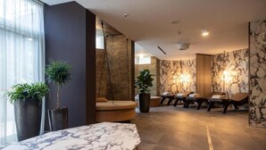 A spa area with a marble reception desk, lounge chairs, and potted plants. - Palace Hotel Città (Arco)