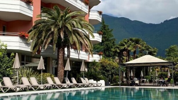 A hotel with a pool, lounge chairs, umbrellas, and a mountain view. - Palace Hotel Città (Arco)