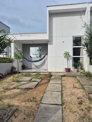 A modern house with a concrete exterior, a hammock, potted plants, and a paved garden area.