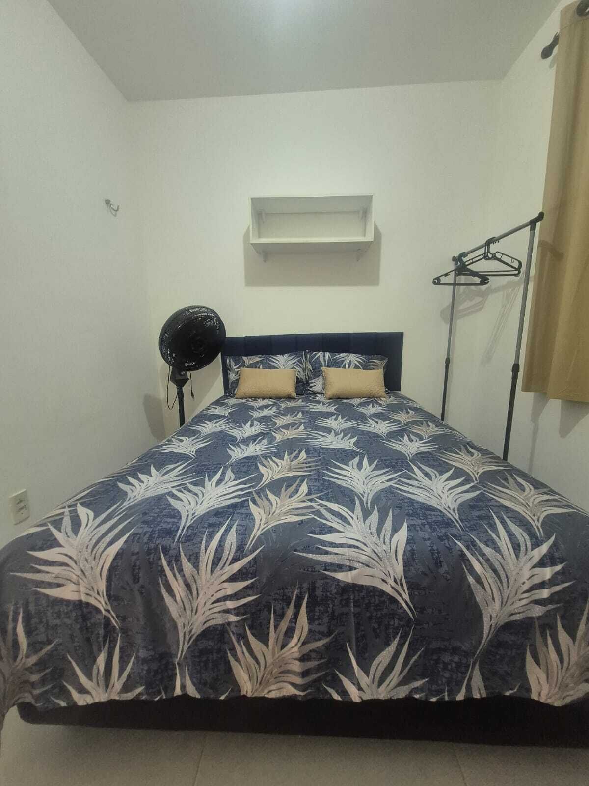 Een slaapkamer met een bed, een plafondventilator, een wandplank en een kledingrek.