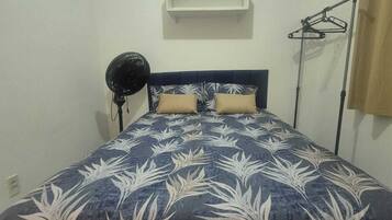 Een slaapkamer met een bed, een plafondventilator, een wandplank en een kledingrek.