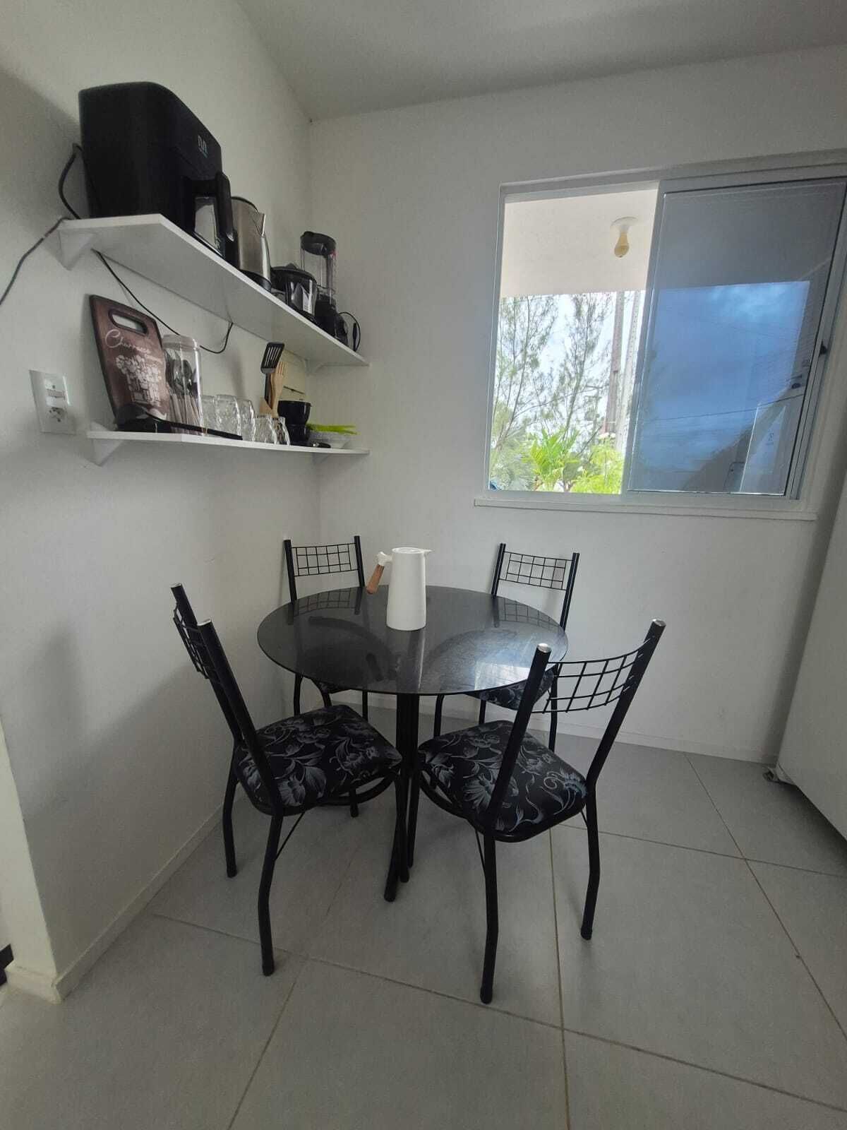 Un área de comedor con una mesa redonda y cuatro sillas, una cafetera y una ventana con vistas a árboles.