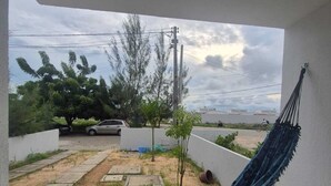 A hammock on a balcony with a view of a residential area, including a car and trees. - Complete house 15 minutes from beaches in Aquiraz (Tapera)