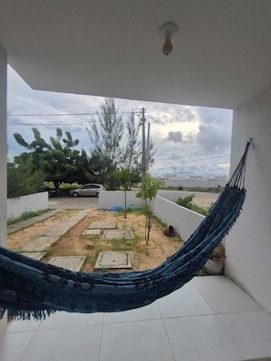 Un hamac sur un balcon donnant sur un quartier résidentiel, avec une voiture et des arbres visibles.
