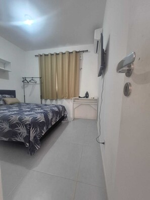 Une chambre à coucher avec un lit, un bureau, une télévision et une fenêtre avec des rideaux.