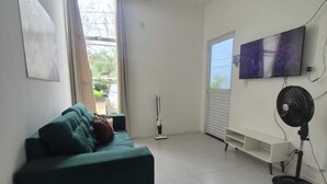 A living room with a teal sofa, a standing fan, a TV, and a window with curtains. - Complete house 15 minutes from beaches in Aquiraz (Tapera)