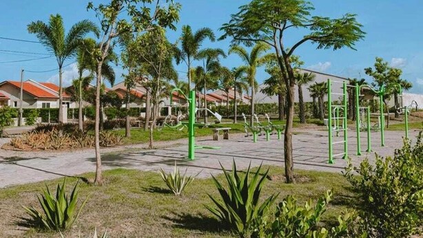 A park with exercise equipment, palm trees, and a building with red roofs in the background. - Complete house 15 minutes from beaches in Aquiraz (Tapera)