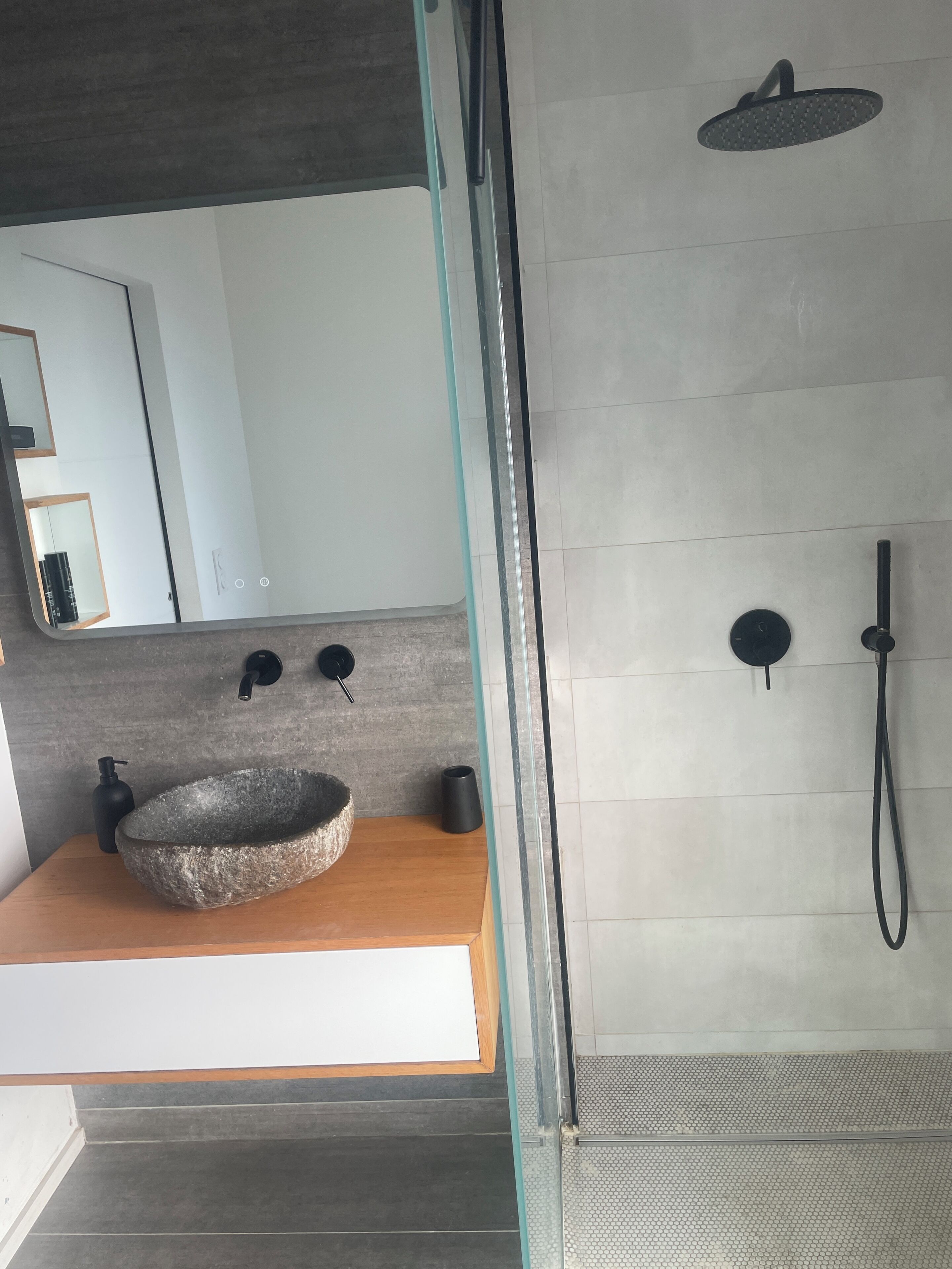 Un baño moderno con lavamanos de piedra, ducha de mano y zona de ducha con mampara de vidrio.