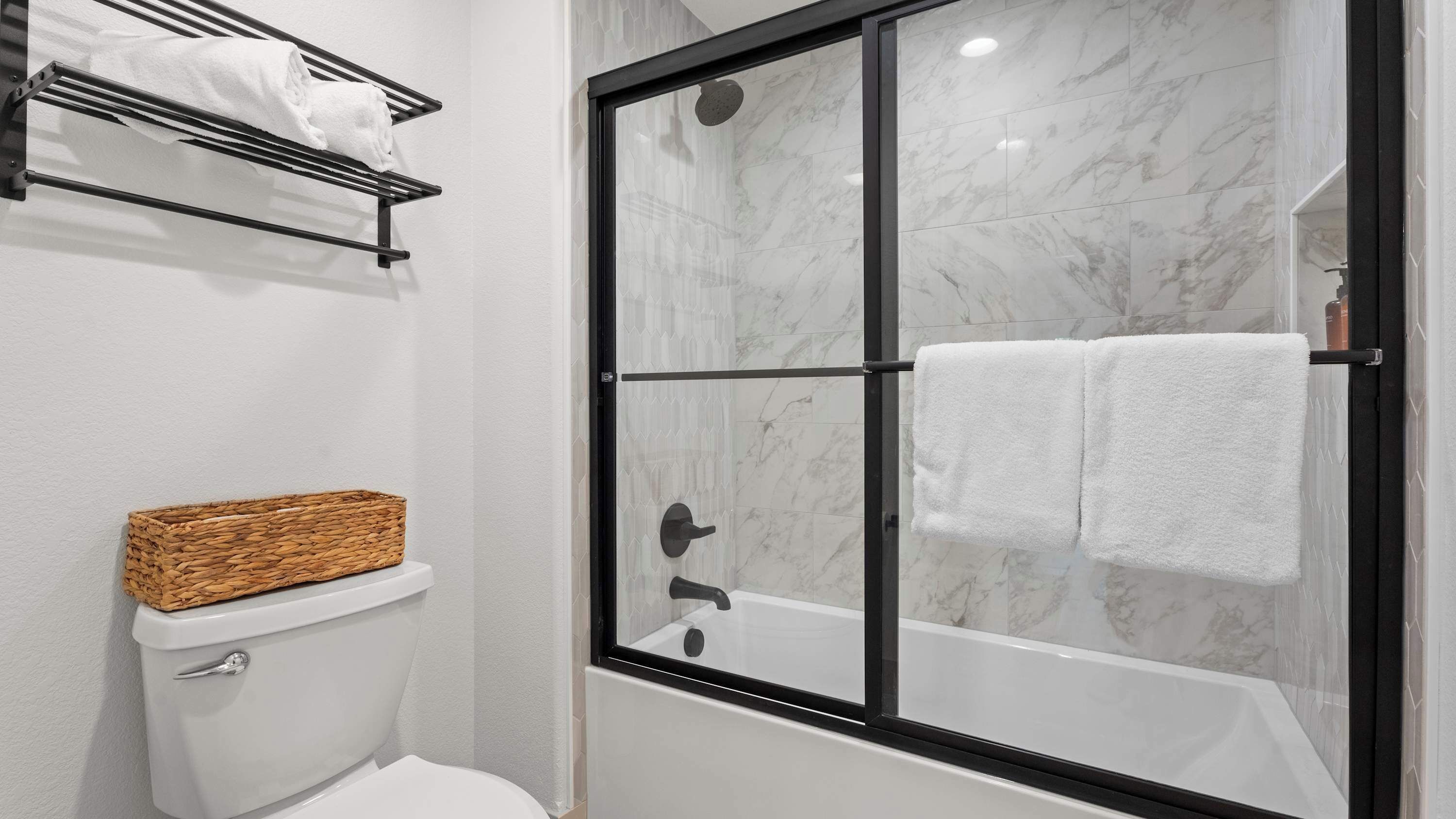 A modern bathroom with a glass-enclosed shower, a toilet with a basket, and a towel rack.
