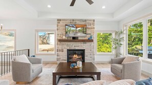 A living room with a stone fireplace, a television mounted above it, and a view of a deck and outdoor area.
