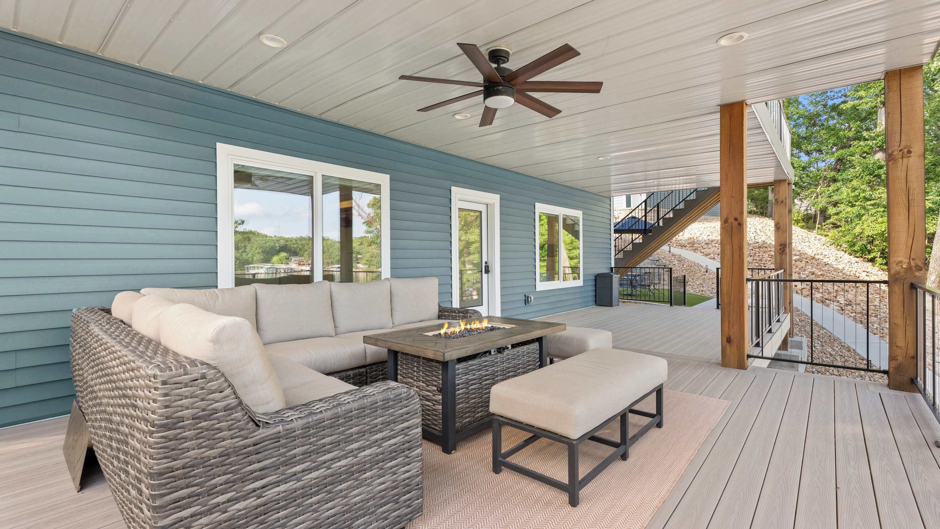 Um deck externo com um sofá, uma mesa com lareira e um ventilador de teto.