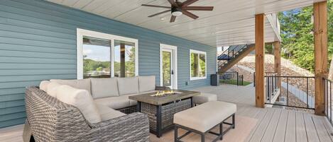 Um deck externo com um sofá, uma mesa com lareira e um ventilador de teto.